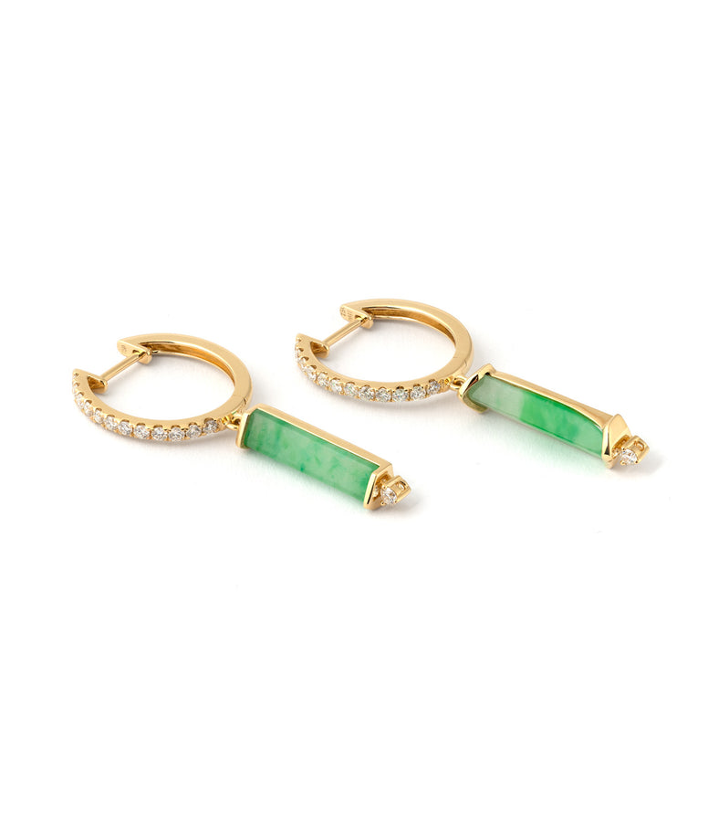 This picture shows one pair of earrings. They are laying down sideways. The earrings are in 18K yellow gold, there is a hoop with diamonds and underneath the hoop is a dangling thin elongated jadeite with a diamond at its bottom